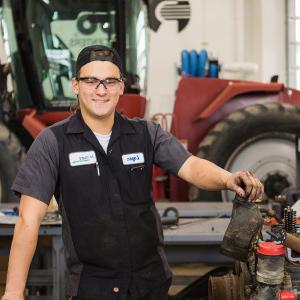 A student poses in front of a tractor inside 学习's Diesel Equipment Technology lab